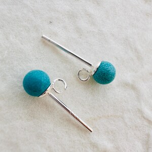 May include: A pair of silver stud earrings with turquoise round beads. The earrings have a post and a small loop on the back.