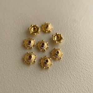 以下が含まれることがあります： 装飾的な波状の縁を持つ、金色の金属製のビーズキャップが8つ。キャップの中央には小さな穴があります。