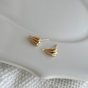 May include: A pair of gold-toned earrings with a shell-shaped design. The earrings are small and delicate, and they would make a great addition to any jewelry collection.