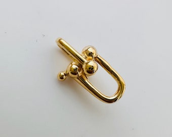 May include: A gold-toned metal clasp with a rounded, open design and three small, round balls. The clasp is a popular style for jewelry and accessories.