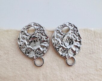 May include: A pair of silver earrings with a textured, organic shape and a circular hoop. The earrings are made of metal and have a modern, minimalist design.