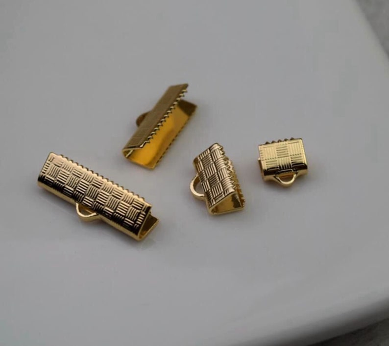 Puede incluir: Cuatro cierres de metal dorado para la elaboraci&oacute;n de joyas. Los cierres tienen una forma cuadrada y una superficie texturizada.