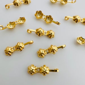 May include: Gold-toned metal flower-shaped embellishments with a loop on one end. The embellishments are designed to be used for jewellery making or other craft projects.