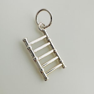 May include: A silver charm in the shape of a ladder. The charm has a loop at the top for attaching to a bracelet or necklace.