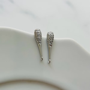 May include: A pair of silver teardrop-shaped earring charms with clear crystal accents.
