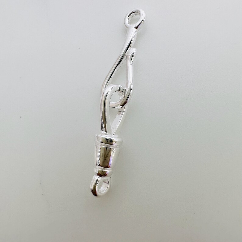 May include: Silver-toned metal clasp with a decorative loop design. The clasp is designed to connect two pieces of jewelry together.