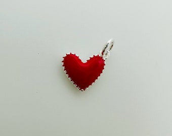 以下が含まれることがあります： ネックレスやブレスレットに取り付けられる、銀色の縁取りと銀色のループが付いた赤いハートのチャームです。