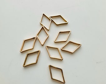 May include: A group of ten gold-colored metal diamond-shaped jump rings. The jump rings are scattered on a white surface.