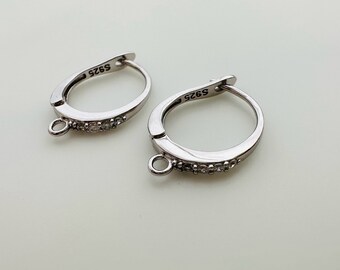 May include: A pair of silver hoop earrings with a clear crystal accent. The earrings are marked with the number "S925" on the back.