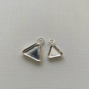 May include: Two silver triangle-shaped pendant settings with a loop at the top. The larger setting is on the left and the smaller setting is on the right.