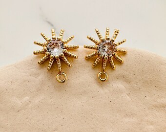 May include: A pair of gold-tone earrings with a starburst design and a clear crystal in the centre. Each earring has a small loop at the bottom for attaching a dangle charm.