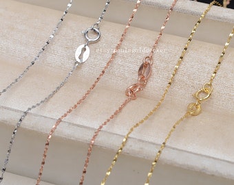 May include: Five delicate gold chains in different colors, including silver, rose gold, and yellow gold. The chains are displayed on a light brown surface. etsypaulagolddecker is visible in the image.