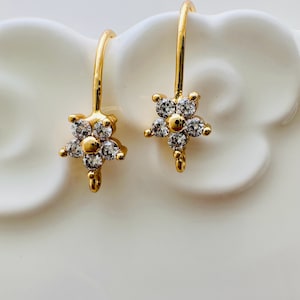 May include: A pair of gold flower-shaped earrings with clear cubic zirconia stones.