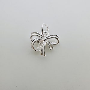 Peut inclure: Un charme en argent en forme de nœud. Le nœud est composé de plusieurs boucles de fil d'argent.