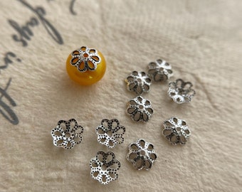May include: A set of eight silver-toned metal flower-shaped bead caps, with one yellow bead in the center. The bead caps have a delicate, openwork design.