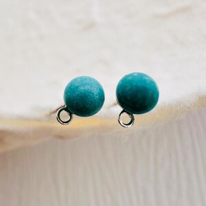May include: A pair of turquoise blue stud earrings with silver posts and loops.