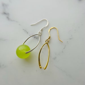 May include: Two dangle earrings. One earring features a silver-tone metal design with a lime green sphere. The other earring has a gold-tone metal design. Both earrings have a hook closure.