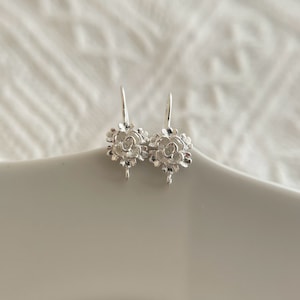 May include: A pair of silver earring findings with a floral design. The findings are in the shape of a flower with a loop at the bottom for attaching earrings.