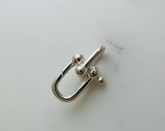 May include: Silver-toned metal clasp with a unique design featuring multiple round balls. The clasp is a U-shape with a rounded opening.