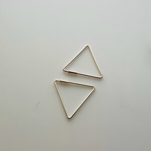 May include: Two gold triangle shaped earrings. The earrings are simple and minimalist.