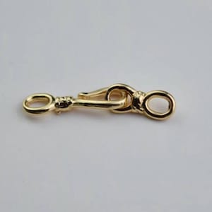 May include: A gold-toned metal clasp with a looped design. The clasp is a connector for a chain or strap.