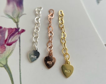 May include: Three heart-shaped charms with a chain attached. The charms are silver, rose gold, and gold. Each charm has the number "925" engraved on it.