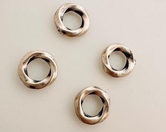 May include: Four silver-toned metal rings with a twisted design. The rings are approximately 2.5 cm in diameter.
