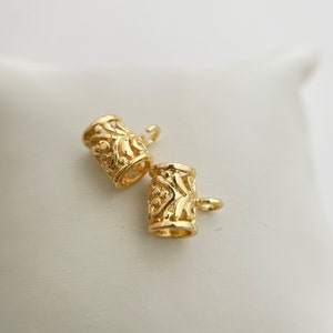 Peut inclure: Deux embouts en métal doré avec des motifs complexes. Chaque embout a une petite boucle pour l'attacher à un cordon ou une chaîne.