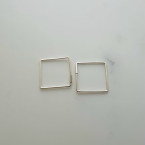 Könnte beinhalten: Ein Paar silberne quadratische Creolen. Die Ohrringe sind schlicht und minimalistisch im Design.