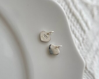May include: Two silver heart-shaped charms with a jump ring for attaching to a necklace or bracelet. The charm on the left has the number "925" engraved on it.