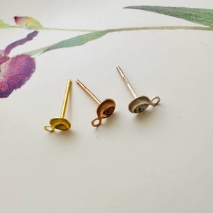May include: Three earring posts with a loop on the back. The posts are gold, rose gold, and silver.