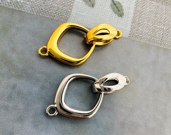May include: Two metal clasps, one gold and one silver, with a square shape and a decorative loop. The clasps are designed for jewellery making.
