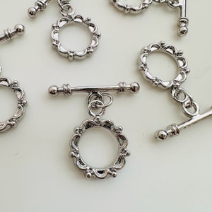 May include: Silver-toned metal clasps with a decorative circle design. Each clasp has a toggle bar and a ring.