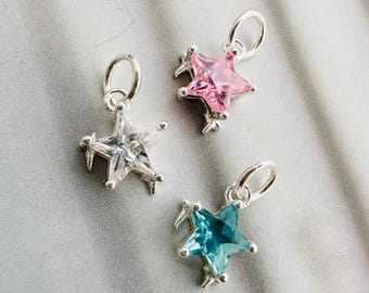 May include: Three star-shaped charms with silver-colored metal settings. One charm features a clear stone, another a pink stone, and the third a blue stone. Each charm has a small loop for attaching to a chain or bracelet.