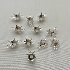 May include: Silver-toned metal settings for rhinestones or other embellishments. Each setting has six points and three loops for attaching to a project.