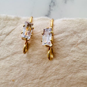 以下が含まれることがあります： 透明な長方形の宝石が付いた、金色のフープイヤリングのペアです