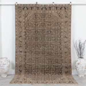 May include: A large rectangular area rug featuring a dark brown and light beige intricate floral and geometric pattern. The rug has a wide decorative border with repeating motifs and a dense, symmetrical design covering the central field area.