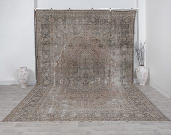 Puede incluir: Una alfombra rectangular grande, de aspecto envejecido, con un patrón tradicional y ornamentado en tonos marrones, beige y grises. La alfombra se exhibe sobre un fondo blanco, mostrando su intrincado diseño y apariencia envejecida. El tamaño de la alfombra es sustancial, cubriendo una gran área.