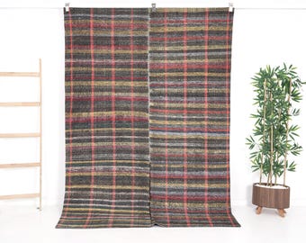 May include: Two rectangular, woven panels with a plaid pattern in shades of brown, red, yellow, and gray. The panels are hanging from a white rod. A wooden ladder and a potted plant are in the background.