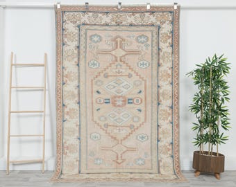 Könnte beinhalten: Ein großer rechteckiger Teppich mit einem zentralen Rautenmuster in gedeckten Pfirsich-, Hellblau- und Cremetönen. Der Teppich hat eine breite dekorative Bordüre mit geometrischen Motiven und stilisierten floralen Elementen im gesamten Design.
