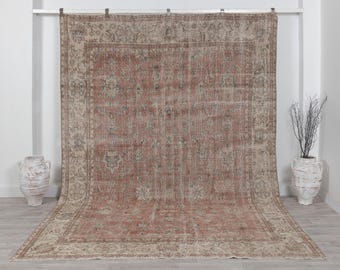 Puede incluir: Una alfombra rectangular grande que presenta un campo central de color rojo terracota descolorido con intrincados patrones florales y de enredaderas en tonos azul, beige y crema apagados. Tiene un borde ancho y detallado.