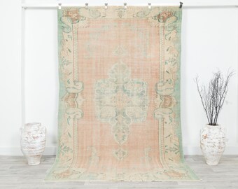 May include: A large, rectangular, vintage rug with a faded, distressed appearance. The rug features a central medallion design in shades of peach, teal, and cream, with a detailed border. The rug is displayed against a white wall.