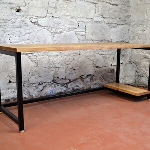 May include: A wooden desk with a black metal frame and a small shelf. The desk has a natural wood finish and the metal frame is black with brass accents.