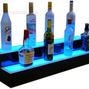 May include: A black, two-tiered liquor display shelf with blue LED lighting. Several bottles of liquor are arranged on the shelves, including vodka, whiskey, and wine. The display is designed to showcase bottles.