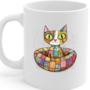 May include: White ceramic mug with a colourful illustration of a cat in a patchwork bed. The cat has large green eyes and a blue collar. The mug is a standard 325 ml size.