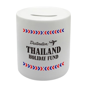 May include: White ceramic money box with a slot on top. It features a red, white and blue design with the text "Destination: THAILAND HOLIDAY FUND".