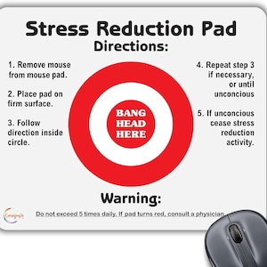 May include: A white mouse pad with a red circle in the centre. The circle has a white inner circle with the text "BANG HEAD HERE" in black. The mouse pad has instructions for stress reduction, including "Remove mouse from mouse pad", "Place pad on firm surface", "Follow direction inside circle", "Repeat step 3 if necessary, or until unconscious", and "If unconscious cease stress reduction activity". The mouse pad also has a warning that reads "Do not exceed 5 times daily. If pad turns red, consult a physician."