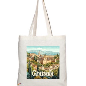 May include: A white canvas tote bag featuring a vintage-style image of the Alhambra palace in Granada, Spain. The image is in a rectangular frame with the text "Granada" printed below it in a retro font.