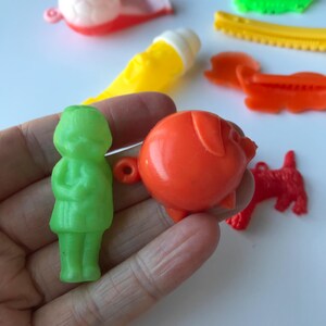 May include: A set of vintage plastic toys, including a green girl doll, an orange pig, and a red dog. The toys are all small and have a retro look.
