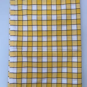 May include: A fabric textile featuring a repeating grid pattern of yellow and white squares. The design is defined by thin, crisp black lines that intersect to form a consistent checkerboard layout across the entire surface of the material.